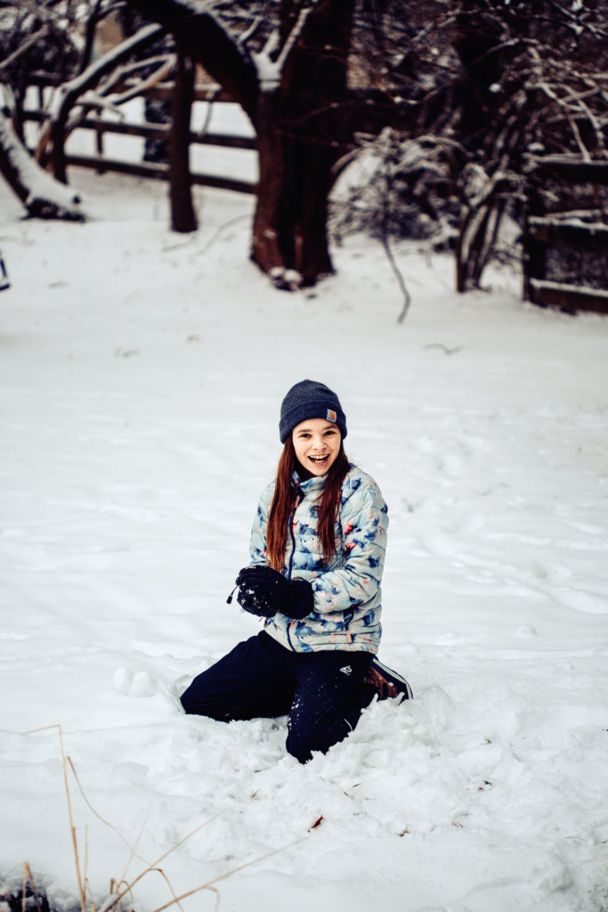 girl playing in the snow building a snowman
